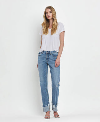 A woman with long blonde hair stands against a plain white background. She's wearing a white t-shirt, Dezie Mid Rise Cuffed Straight Jeans in soft stretch denim with slight distressing from Lovervet by VERVET (available in sizes 1-24), and silver heeled sandals. Her gaze is relaxed as she looks directly at the camera.