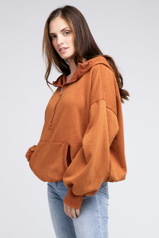 A person wearing a stylish Burke Quarter Zip Stitch Detailed Elastic Hem Hoodie by Western Edge Boutique stands against a plain background. Their long brown hair complements the fashion-forward ensemble, completed by light blue jeans, with hands comfortably tucked in the hoodie's front pocket.