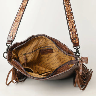 An *American Darling* Large Crossbody Simple Leather with Fringe. It features a brown leather exterior adorned with an intricate floral design on the strap, fringes for a bohemian flair, and an open interior showcasing a yellow fabric lining with writing, brown trims, a small zippered pocket, and multiple compartments.