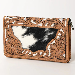 The Percie Cowhide Tooled Wallet by American Darling features a rich brown leather exterior with embossed floral designs and a central panel of black and white cowhide. The wallet includes a zipper closure on the right side, while the intricately tooled leather detailing and texture offer a rustic, Western aesthetic that is perfect for enthusiasts of hide on hair bags.