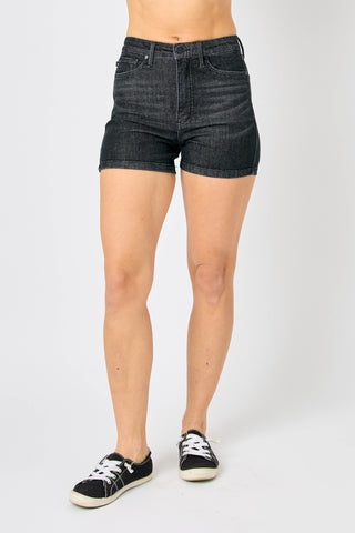 A person wearing the HW Tummy Control Washed Black Shorts from Western Edge Boutique and black sneakers with white soles stands against a plain white background. The image emphasizes the lower half of the body, accentuating the relaxed fit of these stylish shorts.