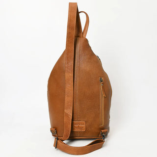 The Collins Brown Cowhide Leather Sling Handbag by American Darling is displayed standing upright against a plain white background. The bag features a single, wide shoulder strap and has an adjustable design. A logo is embossed on one side, and there is also a zippered pocket visible on the other side, showcasing its unique style.