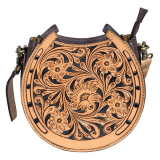 Introducing the Bliss Horseshoe Tooled Canteen Purse by American Darling: a beautifully crafted round purse made of genuine leather, featuring elaborate floral and leaf patterns. This bag boasts a rich tan color complemented by darker brown accents and stitching. Its detailed craftsmanship is highlighted with a buckle strap and metal studs outlining the edges.