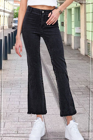 A person wearing comfortable Rustlyn Black Pants from Western Edge Boutique and a white crop top stands on a cobblestone street. The view is from the shoulders down, displaying their outfit and white sneakers. Buildings and bollards line the sides of the street in the background.