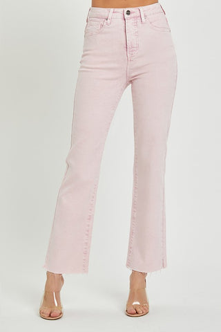 A person is wearing Risen's Pearce Pink Curvy High-Rise Raw Hem Slit Straight Pants, crafted from a soft cotton-spandex blend. The pants feature a front button and zipper closure, along with front and back pockets. The person is also wearing clear heeled shoes against a simple white background.