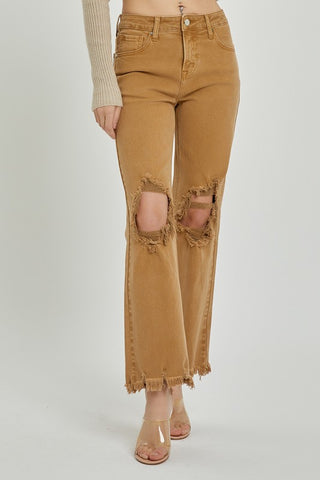 A person is modeling the Risen Maybelle High-Rise Distressed Straight Crop Pants, which are mocha-colored and made from soft cotton, featuring large ripped holes at the knees and frayed hems. They are wearing a long-sleeved ribbed beige top and transparent high-heeled shoes against a plain, light-colored background.