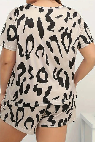 A person is seen from the back, wearing the Landon Leopard Lounge Set Curvy from Western Edge Boutique. This plus size loungewear set features bold black abstract shapes resembling an artistic take on leopard print. The light-colored pajama outfit includes a short-sleeved shirt and tailored shorts, offering a chic yet comfortable look.