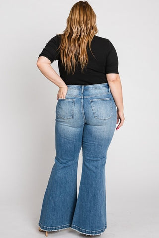 A person with wavy, light brown hair, wearing a black top and light blue Petra153 Cypress PLUS Super High Rise 70s Flare Jeans, stands with their back facing the camera. The image showcases the jeans' vintage-inspired faded detailing and fit against a plain white background.