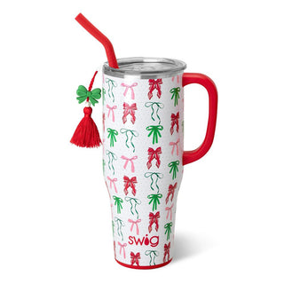 The Christmas Bows tumbler by Western Edge Boutique is a tall, insulated design with a handle and lid, featuring a festive pattern of red and green bows. It includes a matching red straw adorned with a tassel and clover charm, with "swig" printed at the bottom—perfect for adding ribbon-like cheer to your holiday sips!