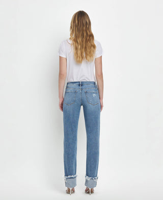 A person with long blonde hair stands facing away, wearing a white short-sleeve T-shirt and Dezie Mid Rise Cuffed Straight Jeans from Lovervet by VERVET in soft stretch denim with distressed flair, complemented by light-colored shoes. The background is plain white.