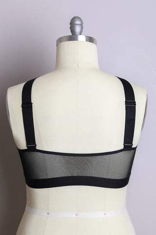 A mannequin showcases the Neena Cross Front Curvy Bralette from Leto Collection from the back. This black bra features wide shoulder straps and a mesh panel along the back, set against a plain, light-colored background.