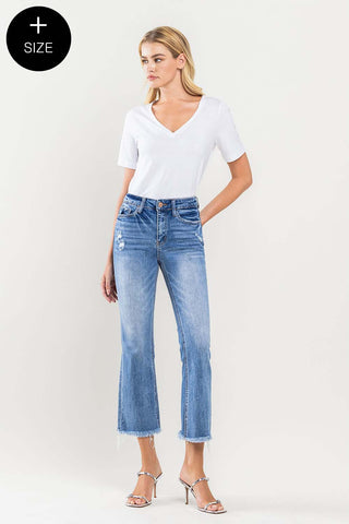 A woman wearing a white V-neck T-shirt and the Nash High Rise Stretch Curvy jeans from Western Edge Boutique, featuring distressed fabric and frayed hems, stands against a plain background. She is also wearing silver high heels.