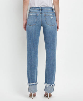 Rear view of a person wearing the Lovervet by VERVET Dezie Mid Rise Cuffed Straight Jeans in soft stretch denim, featuring distressed flair and frayed cuffs. The jeans, available in all sizes 1-24, have two back pockets and are paired with a white top. The person is standing against a plain white background.