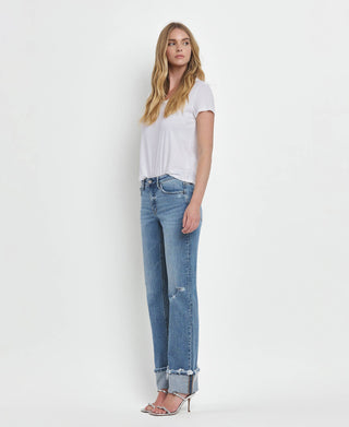 A woman with long blonde hair stands against a white background, wearing a white t-shirt, Dezie Mid Rise Cuffed Straight Jeans All Sizes 1-24 by Lovervet from VERVET in soft stretch denim, and high-heeled sandals. She poses with a relaxed, confident expression, gazing slightly off to the side.