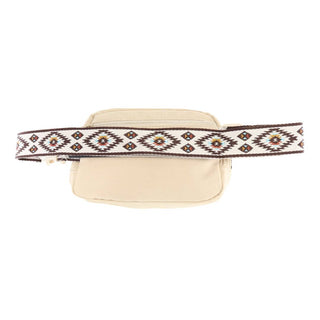 The Cove Aztec Strap C.C Belt Bag by C.C Beanie is a beige belt bag featuring a front zipper pocket and an intricate, multicolored geometric Aztec print strap adorned with brown, white, and yellow diamond shapes.