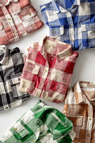 Neatly arranged on a white surface are folded flannel shirts in an array of colors, including urban daisy's Carmel Checkered Flannel-Fall Flannel, available in red, blue, and green plaid patterns. Each stylish piece features buttoned pockets and a classic collar for the perfect autumn look.