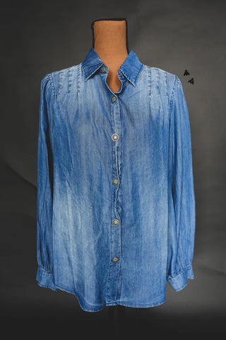 The COWBOY BLUES chambray button-up shirt by 2 Fly is showcased on a mannequin against a dark backdrop. This long-sleeved shirt features a collar, pleated details near the shoulders, and distinctive Aztec buttons that contribute to its unique charm.