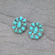 Introducing the Finley Turquoise Concho Stud Earrings from Western Edge Boutique. Each pair showcases turquoise gemstones in a burnished silver setting, featuring a central oval stone encircled by teardrop-shaped stones in a symmetrical, concho stud-inspired design. Presented against a gray, textured background.