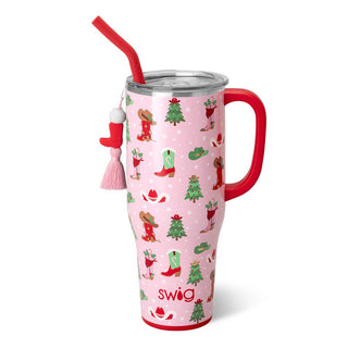 The Howdy Christmas tumbler by Western Edge Boutique is a tall festive tumbler with a Swig design, red handle, and matching straw. It features reindeer, Santa boots, and Christmas tree patterns on a pink background, complete with a pink tassel keychain and small stocking hanging from the straw.