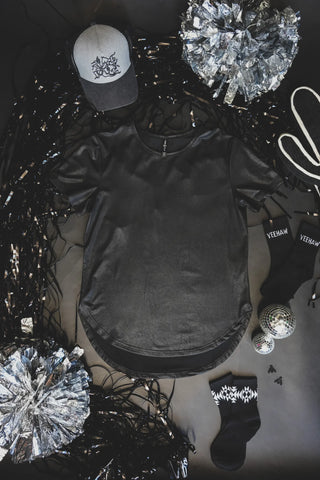 Flat lay of a Swanky Faux Leather Cotton Shirt by 2 Fly, YEEHAW socks, a gray and black hat, two silver cheerleading pom-poms, a pair of black-and-white sneakers, and two small disco balls arranged on a black background. The monochromatic palette with metallic accents adds an extra rad leather lux vibe.