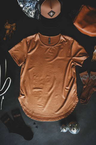 Flat lay of clothing and accessories on a dark surface. Includes a comfy Swanky Faux Leather Cotton Shirt by 2 Fly, stretchy brown socks, a brown and black trucker hat, a copper leather lux pouch, a black bag with white straps, and small decorative items like a miniature disco ball and ornaments.