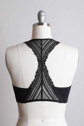 The Skylar Seamless Front Lace Racerback Bralette from the Leto Collection is displayed on a dress form. This black lace bralette features an intricate crisscross lace design on the back, a racerback style, and a snug, supportive band around the bust. Made from Nylon Spandex, it includes removable bra pads for customizable cup fit. The dress form is set against a plain white background.