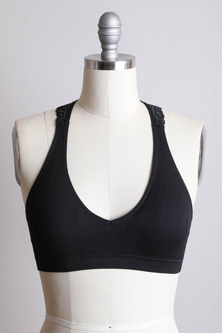 A Skylar Seamless Front Lace Racerback Bralette by Leto Collection, featuring a deep V-neckline, is displayed on a dress form mannequin. This black bralette, crafted from Nylon Spandex, boasts a wide underband and intricate designs on the shoulder straps. It comes with removable bra pads for a customizable cup fit. The background is plain and light-colored.