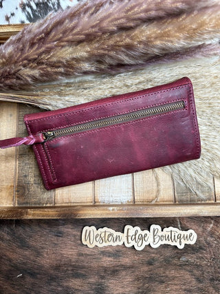 A showstopper quality Red Leather Tooled Wallet by american darling is displayed on a wooden surface. The wallet, surrounded by decorative wheat stalks and fur accessories, catches the eye effortlessly. At the bottom, the text "Western Edge Boutique" can be seen.