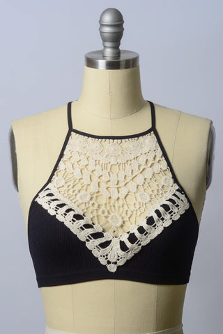 The Reina Crochet Lace High Neck Bralette by Leto Collection is showcased on a beige mannequin torso against a plain background. This stylish piece features intricate cream crochet lace detailing on the front, forming a triangular pattern that beautifully contrasts with the black fabric of the cup fit bralette.