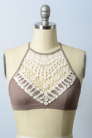 The Reina Crochet Lace High Neck Bralette by Leto Collection, featuring a taupe-colored, ribbed fabric and a cream lace overlay, is displayed on a mannequin. The intricate floral design of the crochet lace extends from the chest to the neckline, creating a high-neck appearance. This stylish bralette stands out against a light blue background.