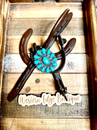 A rustic display featuring the Raleigh Turquoise Stretch Bracelet resting on an antique silver plate shaped like a horseshoe. The wooden background has a brown and tan color scheme. A sticker at the bottom reads "Western Edge Boutique.