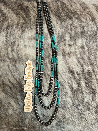 A three-strand necklace from the Ida Navajo Pearl Layered Necklace Set, showcasing alternating turquoise and burnished silver beads, elegantly laid against a textured fur background. A small wooden tag beside it reads "Western Edge Boutique.