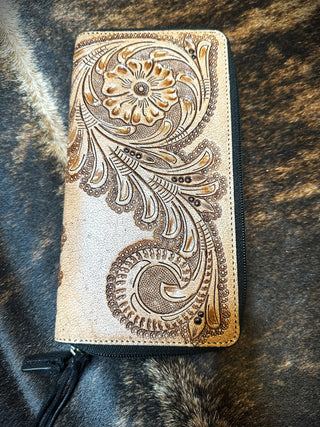 The Rivers Leather Wallet from Western Edge Boutique, featuring an intricate floral and paisley design embossed on its tan leather surface, lies on a fur-textured background. This sandy-colored wallet includes a black zipper along one edge with a sturdy zipper pull.