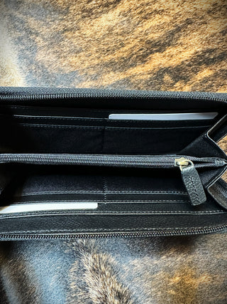 A black Rivers Leather Wallet by Western Edge Boutique is open, revealing two compartments. Each compartment features a slit pocket holding a white card or piece of paper. The wallet is set on a furry surface with brown and black tones.