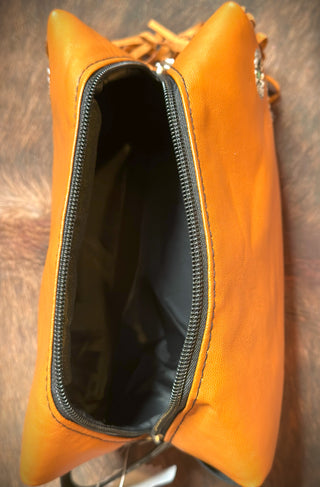 Image of an open orange Kami Pistol Packin' Make-up Bag by 2 Fly, featuring a black interior lining. The picture is taken from a top-down perspective, showcasing the bag's zippered opening. The background appears to be a soft, fur-like surface, adding a touch of luxury to this stylish travel bag.