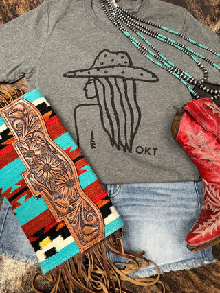 A flat lay image featuring a super soft Western Edge Boutique Harley Gray Cowgirl Silhouette tee, paired with jean shorts, red cowboy boots with intricate designs, a fringed clutch with a Southwestern pattern, and a beaded turquoise necklace—perfect for the modern cowgirl.