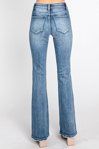 A person wearing Petra153's Ryland Mid Rise Stretch Classic Bootcut Jeans is standing with their back to the camera. The blue jeans feature classic 5-pocket styling and seams running down the back of the legs. The wearer is posed against a plain white background, with their shoes partially visible.