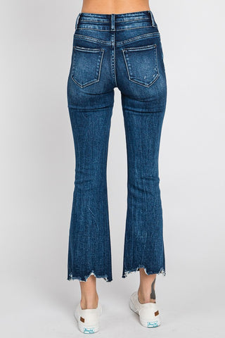 An individual dressed in Petra153's Josslyn High Rise Crop Bootcut Frayed Hem Jeans, featuring back pockets and detailed stitching, paired with white sneakers that display a visible brand logo on the sole, is standing against a plain background.