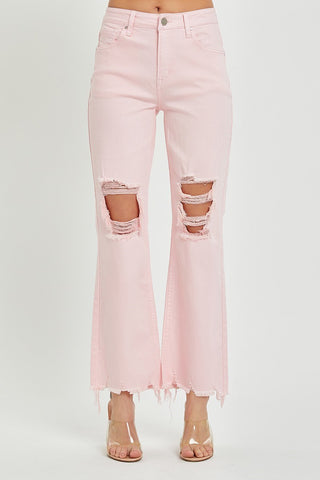 A person is modeling the Pixley Baby Pink High Rise Straight Crop Pants Distressed by Risen. The jeans feature a high-rise fit, wide legs, distressed knees, and frayed hems. They are paired with clear high-heeled shoes. The model's torso is not visible against the plain white background.