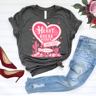 WESTERN EDGE BOUTIQUE's gray Heart Break Motel - Anti Valentine's Day Graphic Tee, featuring a pink heart and "Lonely Street, No Vacancy," pairs perfectly with blue jeans and red heels. Complete the vintage-inspired look with a pink and red rose bouquet against a white backdrop for the anti-Valentine's vibe.