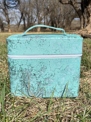 Ideal for any outdoor outing, the Heard your Makeup Tool Box by Western Edge Boutique features a stylish textured turquoise design with a white zipper and convenient top handle. Perfectly placed on green grass in a park, it sits against the backdrop of trees with bare branches beneath a clear sky—truly an essential accessory for storing your essentials.