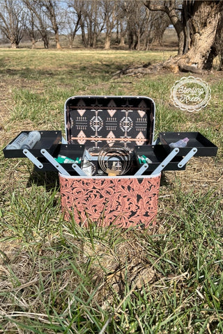 A must-have for artists, this thoughtfully designed open carrying case paired with tattoo equipment is set on grass in a wooded area. Boasting intricate patterns and the "Western Edge Boutique" logo, the Heard Your Makeup Tool Box flawlessly complements the tranquil backdrop of trees and lawn.