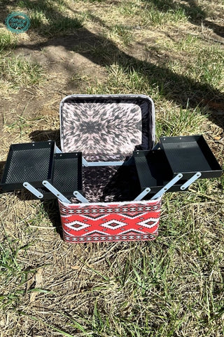 The Heard your Makeup Tool Box by Western Edge Boutique sits open on the grass, its trays extended to reveal a striking geometric red and white design. Shadows play across the ground, accentuating the perfectly organized compartments of this must-have makeup tool box.