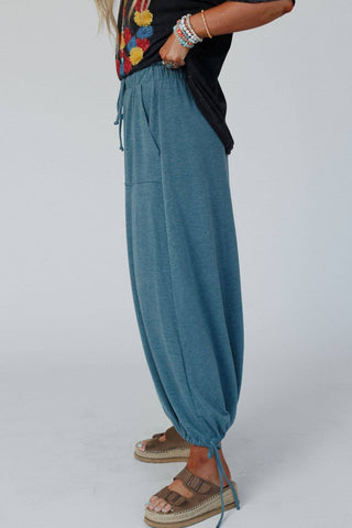 A person wearing the Three Bird Nest Rylie Drawstring Maxi Skirt in a teal boho style, paired with a black top adorned with colorful embroidery. They accessorize with multiple bracelets and brown sandals, standing in a side profile against a plain background, embodying a boho western wardrobe.