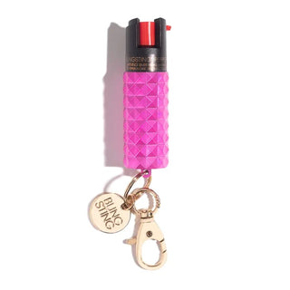 The Emergency Pepper Spray Key Ring by BLINGSTING is a canister of pink pepper spray featuring a textured grip, a keychain loop attached to a clip, and a charming "BLINGSTING" label. This women's safety product includes UV marking dye and has a black top with a red trigger.