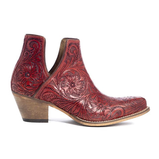 The Moxie Hand-tooled Booties in Scarlet by Myra feature a single red ankle boot with an intricate hand-tooled floral and swirl pattern engraved into the leather. These Western booties are designed with a wooden stacked heel, rounded toe, and deep side cutouts, offering both decorative flair and stylish appeal.