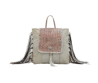 Introducing the chic SMOKEY BACKPACK LEATHER & HAIRON BAG by Myra, showcasing a charming textured light pink flap adorned with an alligator pattern, complemented by a silver button and white tassel. The beige body boasts intricate floral embossing while the sides feature vibrant multicolored fringes. The design includes a convenient small handle on top and luxurious hair-on cowhide accents for an added touch of sophistication.