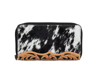 Introducing the **Darrington Ranch Cowhide Tooled Wallet** by **Myra**: a stylish wallet featuring a striking black and white cowhide pattern. It is beautifully accented with an intricately hand-tooled tan leather design at the bottom. This unique hair-on-hide wallet comes with a practical black zipper closure that runs along the top and partially down the sides.