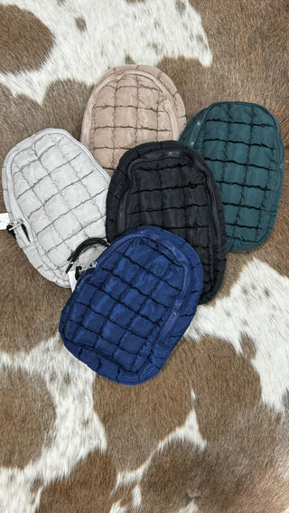 Five Ellison Quilted Crossbody Handbags from Western Edge Boutique, ideal as a women's accessory, are presented in beige, green, black, navy, and gray on a brown and white cowhide surface. The stylish quilted design is showcased as they are arranged in a semicircle.