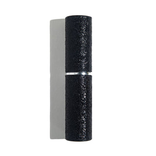 A textured black cylindrical Emergency Mini Stunna from BLINGSTING, featuring a silver band in the middle, casts a shadow on a grayish-white background. The rough surface of this stun gun contrasts with the smooth, reflective band, ensuring both style and women's safety.